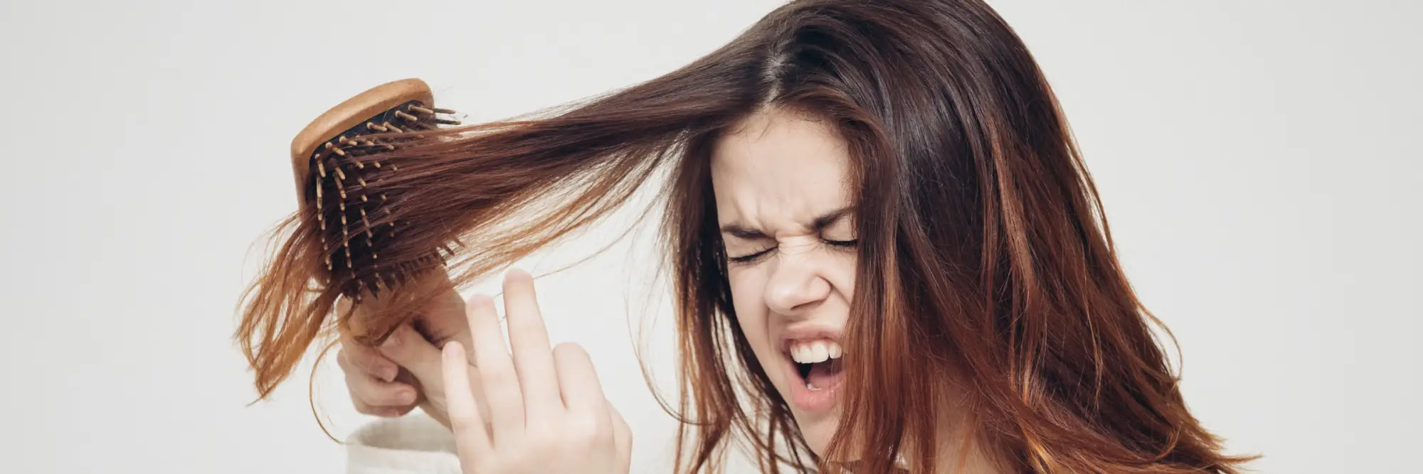 Frustrierte Frau bürstet verfilztes Haar, Problembehandlung für Haarpflege